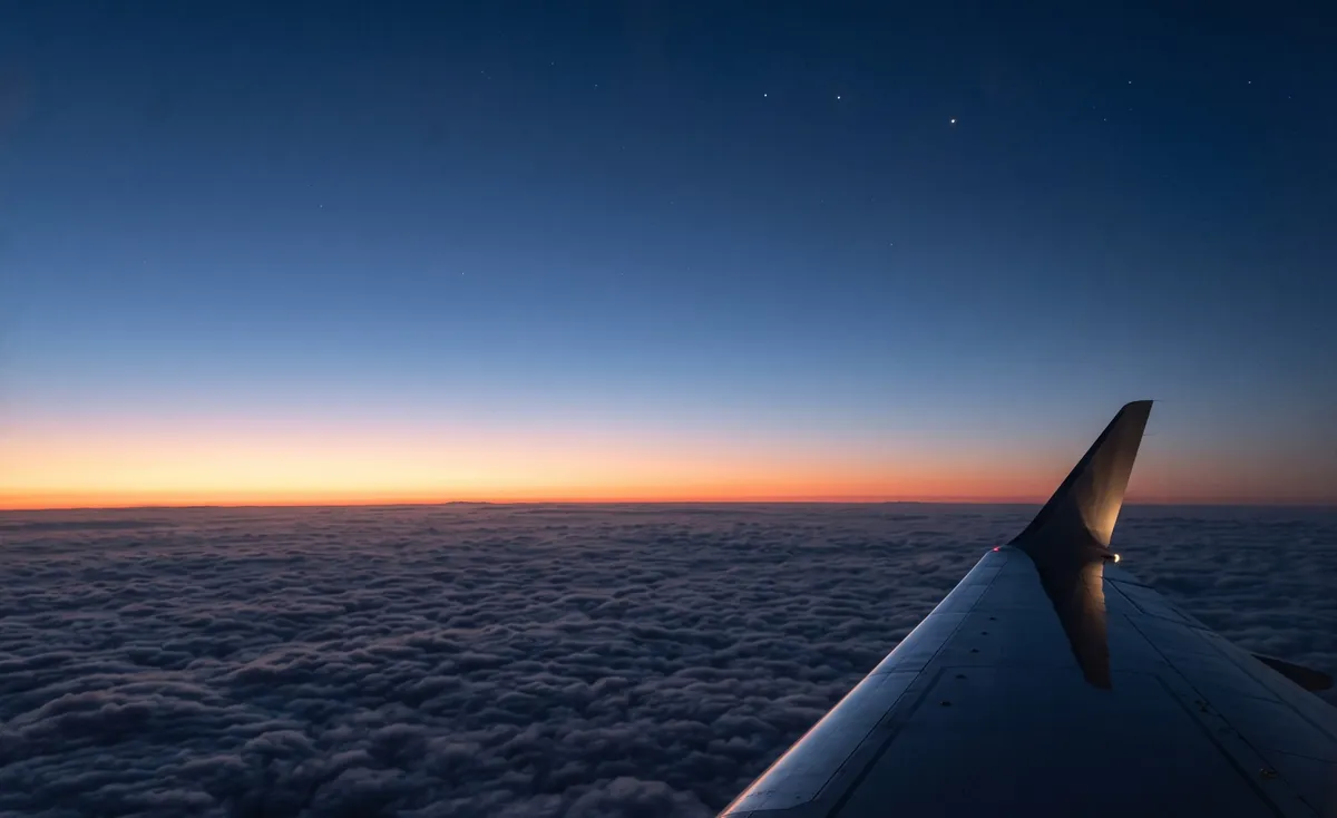 A sea of clouds seen from a private jet at cruising altitude after sunset, the horizon glowing apricot under a deep blue sky